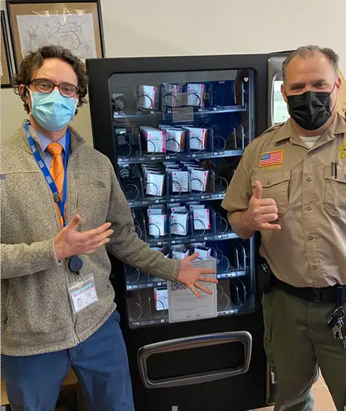 2 men wearing COVID masks in front of a Narcan vending machine at a Marin County jail