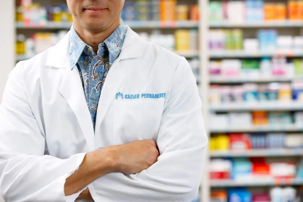 photo of male pharmacist with shelves full of medications in the background