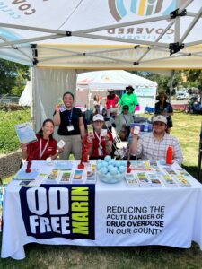 4 people from OD Free Marin's staff booth at the Marin County Fair, providing information pamphlets and free Narcan