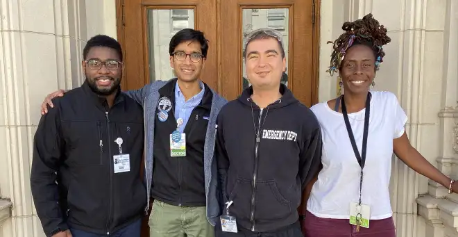 group of 4 people with staff badges and lanyards smiling in front of a doorway